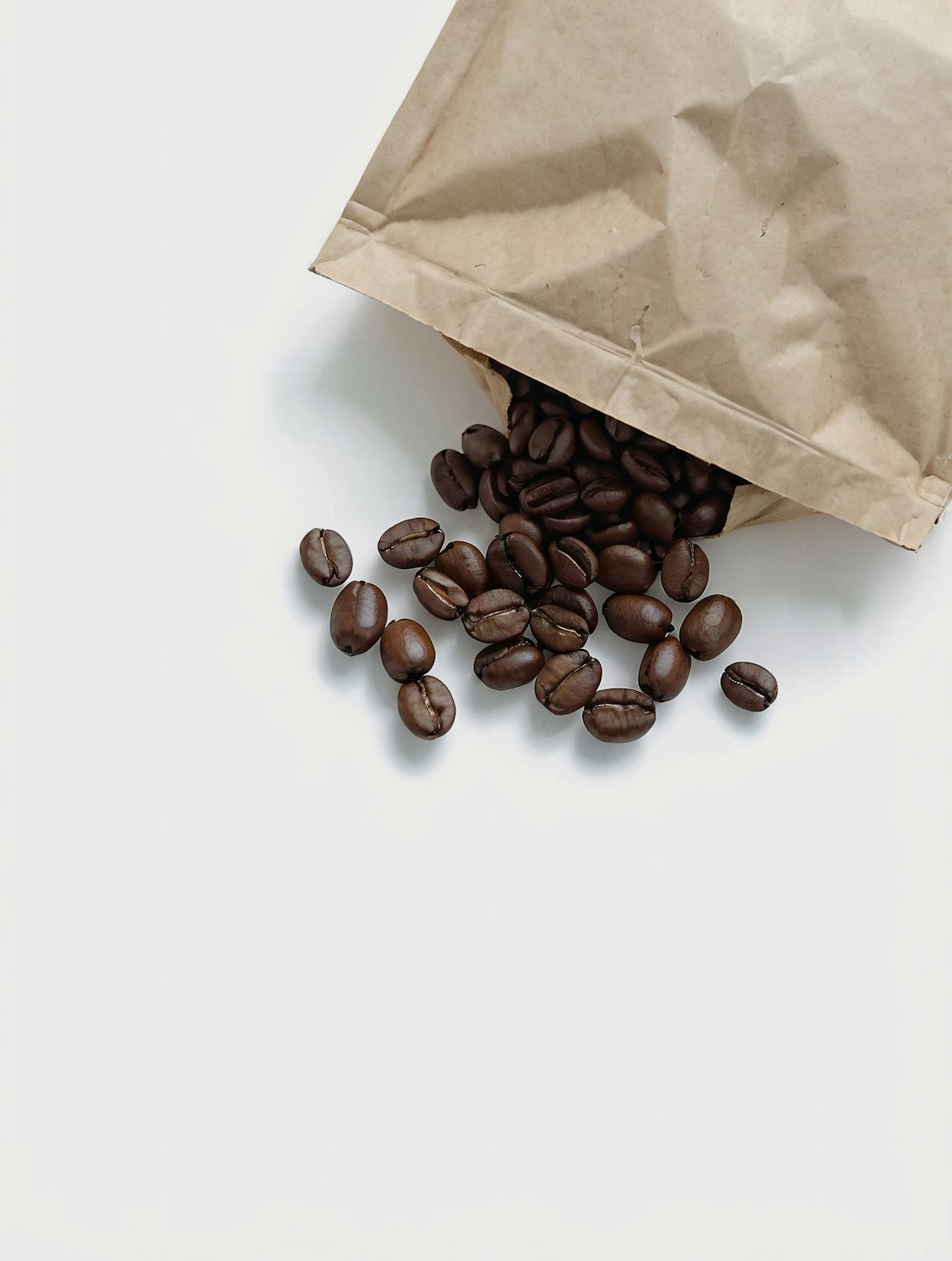 Kraft paper coffee bag spilling dark roasted beans onto a white surface